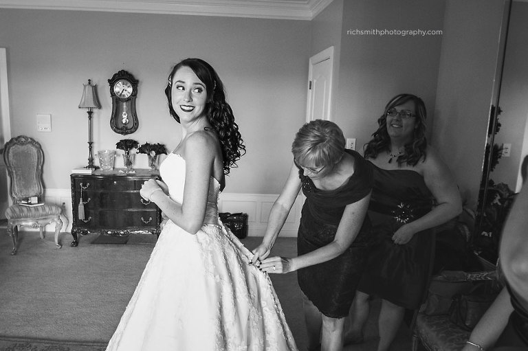 Mom and bridesmaids help bride into wedding gown.
