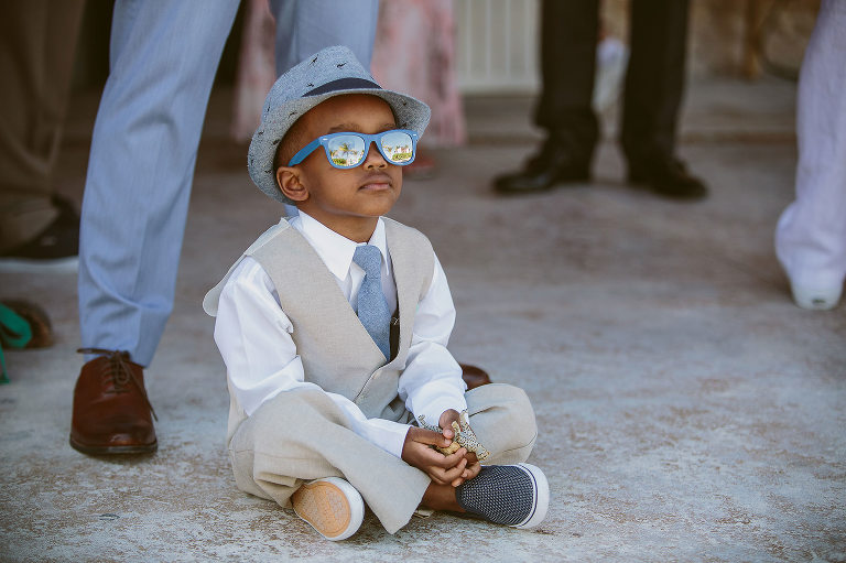 ring bearer sitting on the ground with hat and sunglasses 