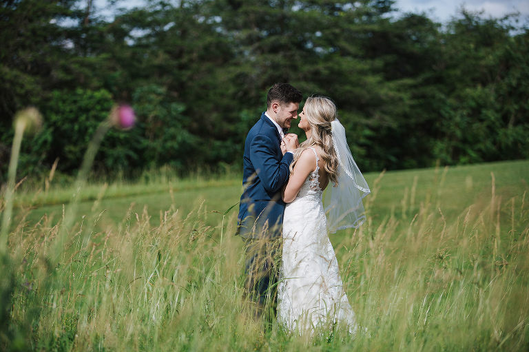 bride and groom in field holding hands