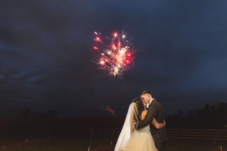 bride and groom kiss during a firework show after their reception