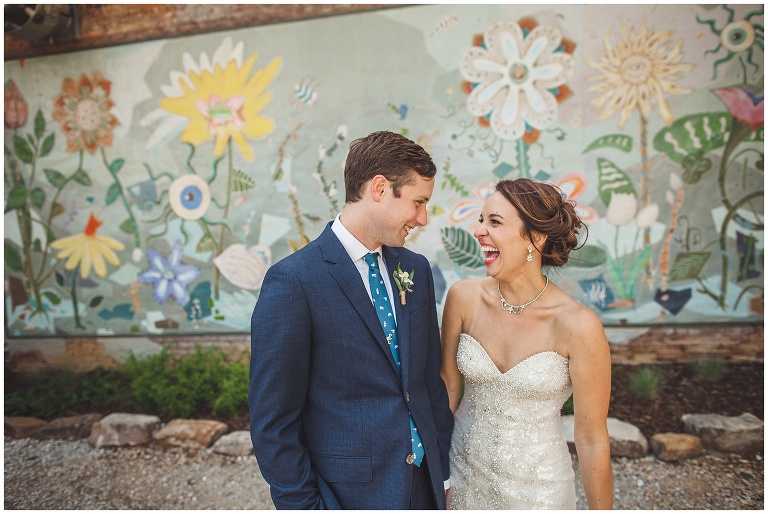 bride and groom laughing in front of mural 
