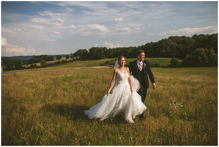 bride and groom walk through field 