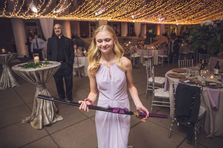 brides sister presenting groom with sword for cutting wedding cake 